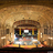 A pixelated image of a building facade with a central arched entrance, flanked by columns and decorative elements, set against a textured brown background.