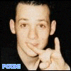 A person with short dark hair and light skin makes a hand gesture near their mouth against a black background, with blue text in the bottom left corner.