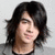 Static pixelated image of a person with long dark hair, light skin, and a neutral expression against a light gray background.