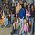 A crowd of people in various poses and clothing, with two individuals wearing blue tops standing prominently among them.