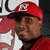 A pixelated close-up of a person wearing a red cap with white trim and a black brim, partially visible red clothing, against a blurred background.