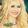 A static image of a smiling person with long wavy blonde hair, wearing a light-colored top with a visible necklace.