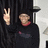 Pixelated image of a person in dark clothing making a peace sign with their right hand, wearing a red collar or scarf.