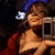 Woman with brown hair and blue headband holds silver camera, smiling in red outfit against dark background.