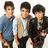 Three young men stand side-by-side in a pixelated image; the central figure wears a white shirt and beige vest, the left figure wears a blue shirt, and the right figure wears a black jacket over a white shirt.