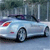 Pixelated static image of a light blue car with dark accents, red taillight, and visible wheel, set against a blurred background.