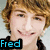 Pixelated portrait of a smiling person with light brown hair, wearing dark clothing and displaying text overlays.