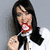 A woman with long dark hair wears a white shirt and red bow tie, holding a lollipop and blowing bubbles in a six- animation