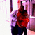 A person in a red top and dark pants stands indoors holding a child, with background elements shifting between frames.