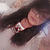 A pixelated close-up of a person's face with long dark hair, showing a hand near the cheek and a blurred background.