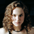 Pixelated close-up of a person with light brown curly hair against a dark background, wearing a light-colored top.