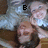 A pixelated image of a person with long dark hair lying on a bed, wearing light-colored clothing and resting their head on a pillow.
