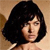 Pixelated close-up of a person with short black hair against a light brown background, wearing a light-colored top.