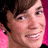 Pixelated image of a person with brown hair and pink background, featuring text overlays in bright pink font on black.