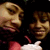 Two people in dark clothing with red accents pose together, one giving a thumbs-up gesture while the other smiles.