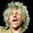 Pixelated close-up of a person with voluminous light-colored curly hair against black background, mouth open in mid-expression.