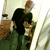 A person in a black shirt and red cap holds another figure while standing near a wooden cabinet with items on top.