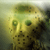 Pixelated static image of a yellowish-green figure with green eyes and dark spots against a gradient background.