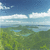 Static pixelated landscape showing blue sky with white clouds, green foliage below, and a distant horizon line.