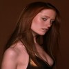 A woman with long brown hair wearing a black sleeveless top, looking downward against a solid brown background.