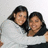 Two people with dark hair wearing white shirts pose closely together against a light background.