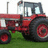 Red tractor with black wheels and silver exhaust pipe on green grass background.