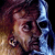 Pixelated static image of a person's face with dark hair and blue-toned lighting against a gradient background.
