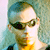A person with short hair appears in three distinct views: wearing sunglasses against a green background, in a dark setting with a brown jacket, and in a light setting with a dark shirt.