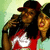 Two people in a red and white shirt pose together, one wearing a maroon cap, against a light green background.