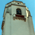 Pixelated image of a light-colored building with a dark window and brown trim against a blue background.