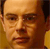 Static pixelated image of a human face with warm brown and orange tones, showing partial facial features including eyes, nose, mouth, and hair against a dark background.