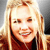 A static pixelated image of a person with long blonde hair, light skin, and a dark top, smiling with visible teeth against a gradient background.