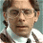 Pixelated close-up of a person with short brown hair wearing a white shirt against a light blue background.