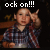A child in a blue and red plaid shirt makes a rock-on gesture with their right hand, positioned against a dark background with faint yellow shapes.