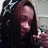 Pixelated image of a person with long dark hair holding an object, wearing dark clothing against a light background.