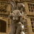 A pixelated animation of a stone gargoyle perched on an ornate building facade, with white highlights on its wings and body.