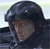Pixelated static image of a person wearing a dark helmet and jacket against a light background, with visible dithering and low-resolution rendering artifacts.