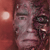 Pixelated close-up of a human face with dark hair and eyes against a reddish-brown background, featuring visible dithering and low-resolution rendering artifacts.
