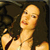 Pixelated image of a person with light skin tone, long dark hair, and a bare shoulder, set against a dark background.