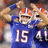 Pixelated image of a person in blue sports uniform with number 15, orange helmet stripes, and another figure partially visible behind.