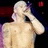 Static pixelated image of a shirtless figure with light skin and short hair, holding an object near the face against dark background with red and purple elements.
