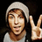 Pixelated image of a person wearing light gray beanie and white shirt, making peace sign with right hand against dark background.