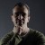 Pixelated image of a person with short brown hair wearing a dark green shirt against a gradient gray background.