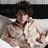 A person with dark curly hair wearing a light-colored patterned shirt sits on a white couch against a black headboard, shifting posture across frames.
