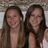 Two people with long brown hair stand side-by-side against a blurred background, both smiling.