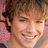 Pixelated close-up of a smiling person with curly brown hair against a pinkish background.