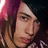 Pixelated close-up of a person with long brown hair and pink highlights, wearing dark clothing against a dark background.
