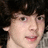 Pixelated close-up of a person with dark hair, light skin, and a neutral expression against a dark background.