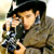 Static pixelated image of a person in military-style attire holding a firearm, with visible facial features and partial uniform details.