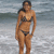 A woman in a black bikini stands on a beach with waves behind her, shifting stance across frames.